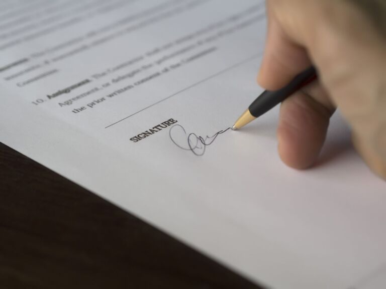 Une main signe un contrat formel avec un stylo sur un bureau en bois.