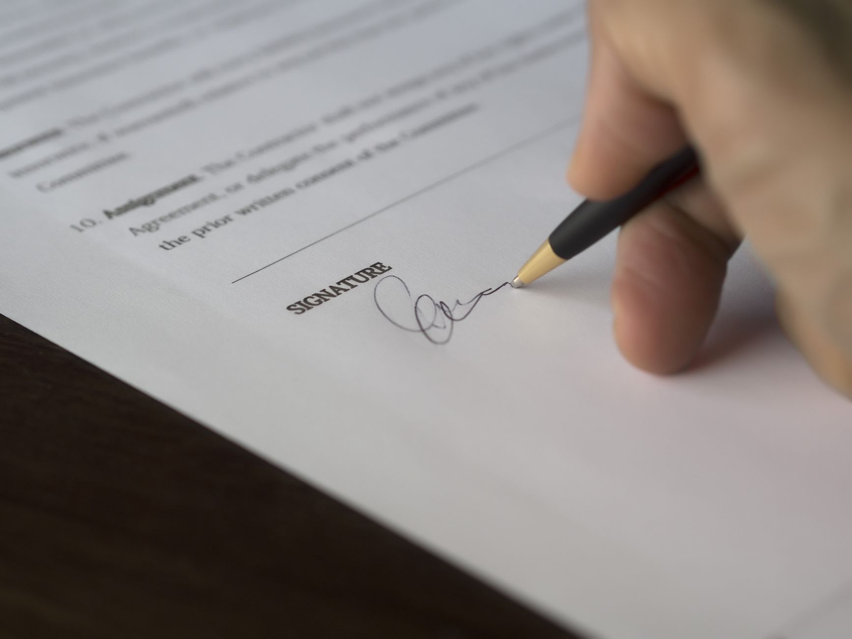 Une main signe un contrat formel avec un stylo sur un bureau en bois.
