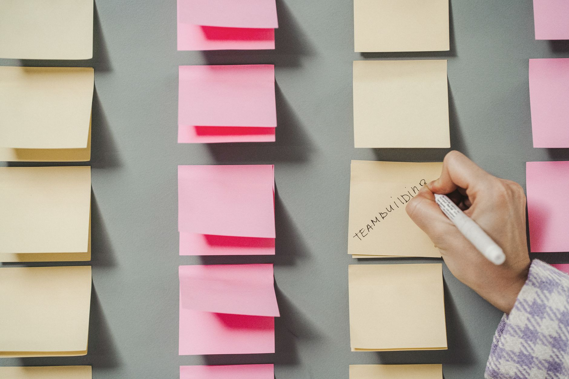 Un gros plan d'une main écrivant 'team building' sur des post-it pastel, illustrant l'organisation et la planification.
