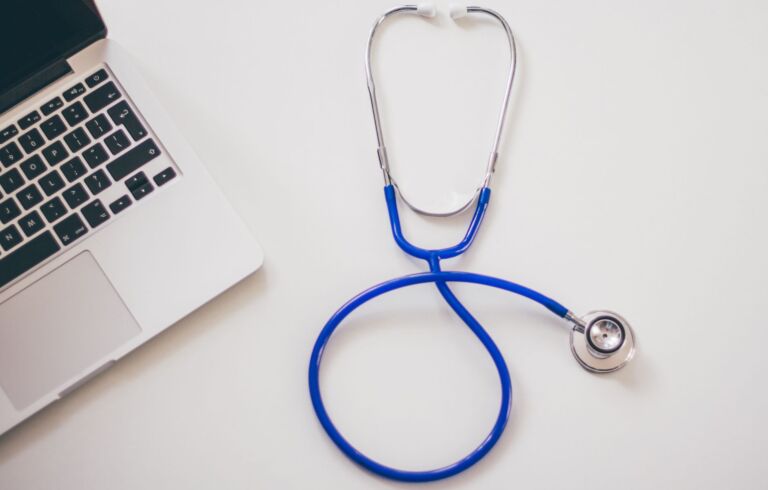 Stéthoscope médical et ordinateur portable sur un bureau blanc, symbolisant les solutions de santé numérique.