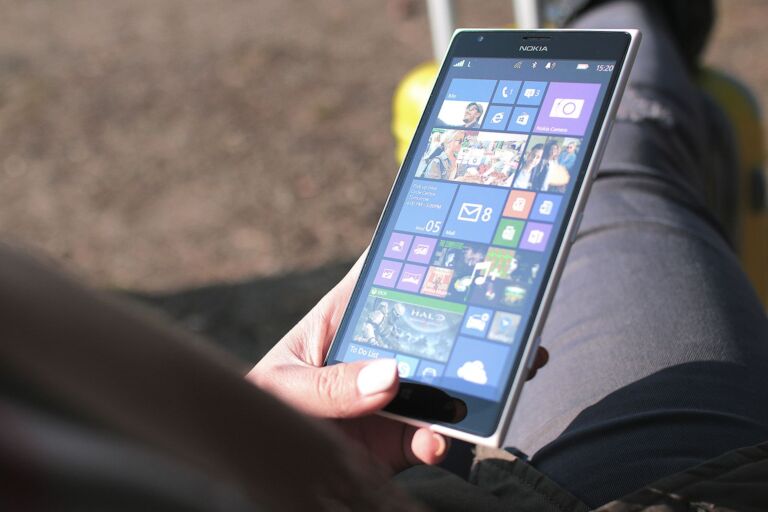 Gros plan sur une femme tenant un smartphone Nokia fonctionnant sous le système d'exploitation Windows en extérieur, montrant l'interface tactile.