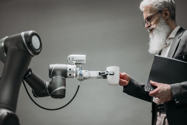 Un homme âgé reçoit une tasse d'un bras robotique dans un bureau moderne.