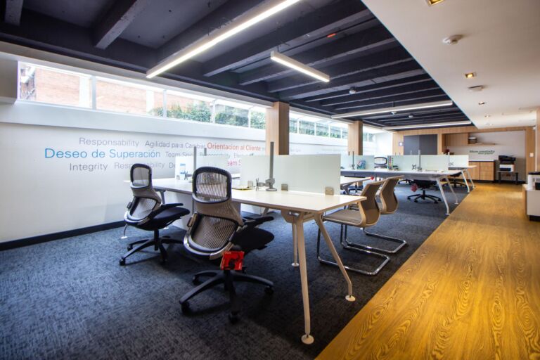 Un espace de bureau moderne et bien éclairé avec des chaises ergonomiques, des tables et des cloisons en verre.