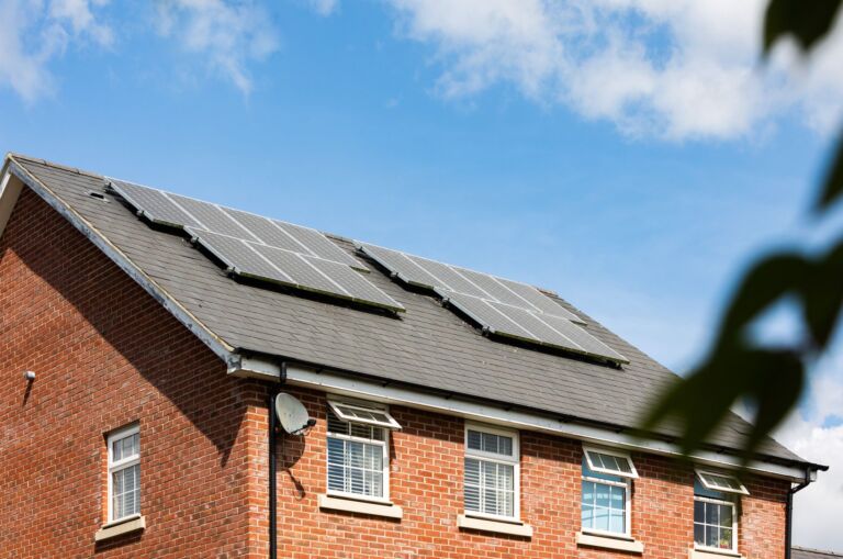 Maison en briques avec des panneaux solaires sur le toit sous un ciel bleu clair, promouvant l'énergie durable.