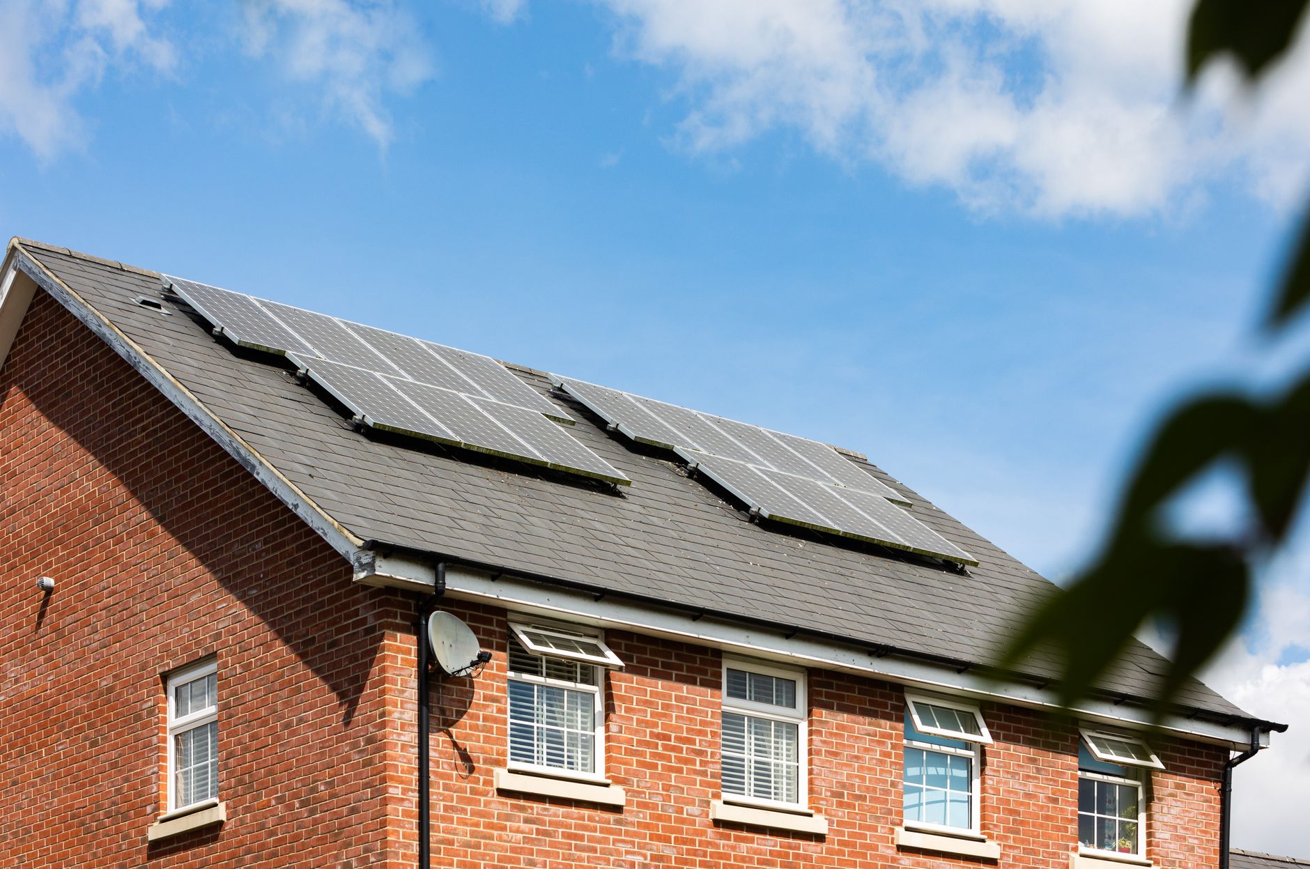 Maison en briques avec des panneaux solaires sur le toit sous un ciel bleu clair, promouvant l'énergie durable.