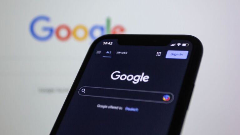 Écran de smartphone affichant la recherche Google en mode sombre avec le logo Google en arrière-plan.