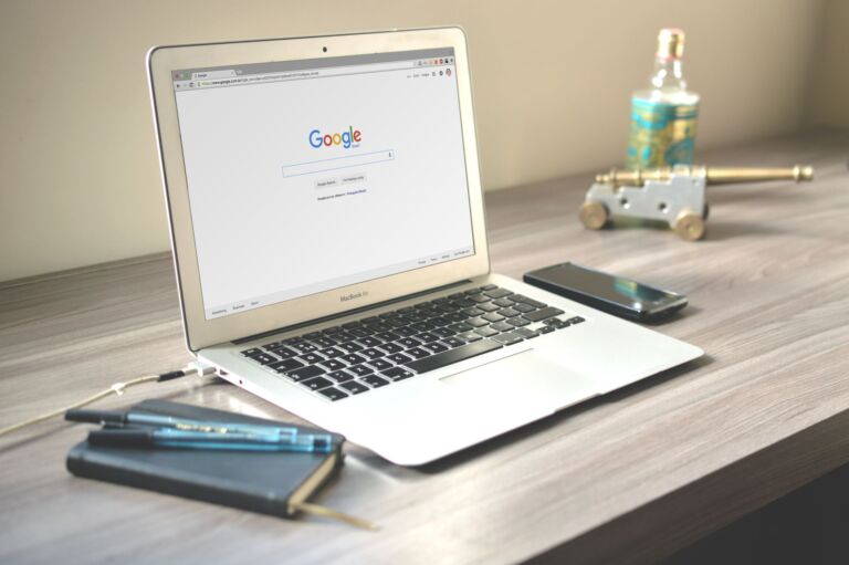 Un bureau soigné avec un ordinateur portable affichant une recherche Google, un smartphone et un carnet sur un bureau en bois.