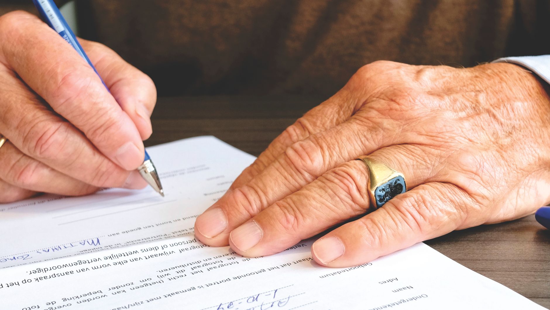 Gros plan d'un senior signant un document légal, mettant l'accent sur la main et l'alliance en or.