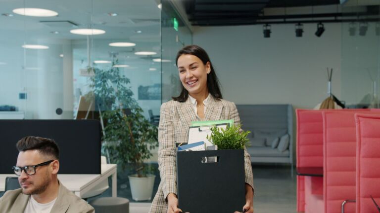 Une femme d'affaires heureuse transporte ses affaires et une plante dans un bureau moderne.