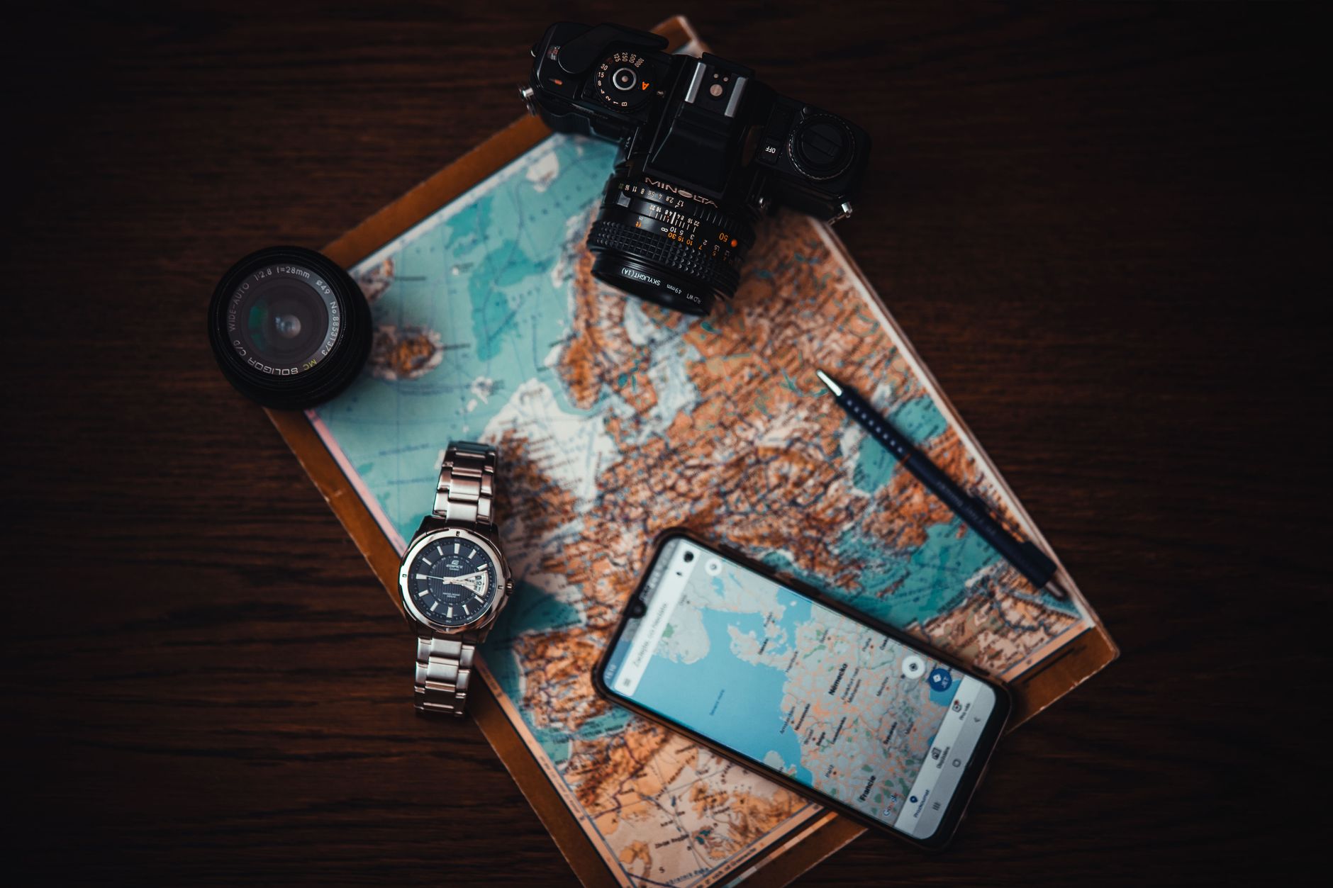 Vue du dessus des essentiels de voyage comprenant une carte, un appareil photo, un téléphone, une montre et un objectif sur une surface en bois.