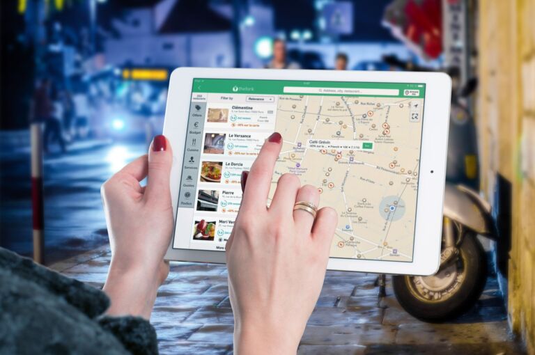 Des mains utilisant une carte numérique sur une tablette dans un milieu urbain la nuit, illustrant la navigation et la technologie.