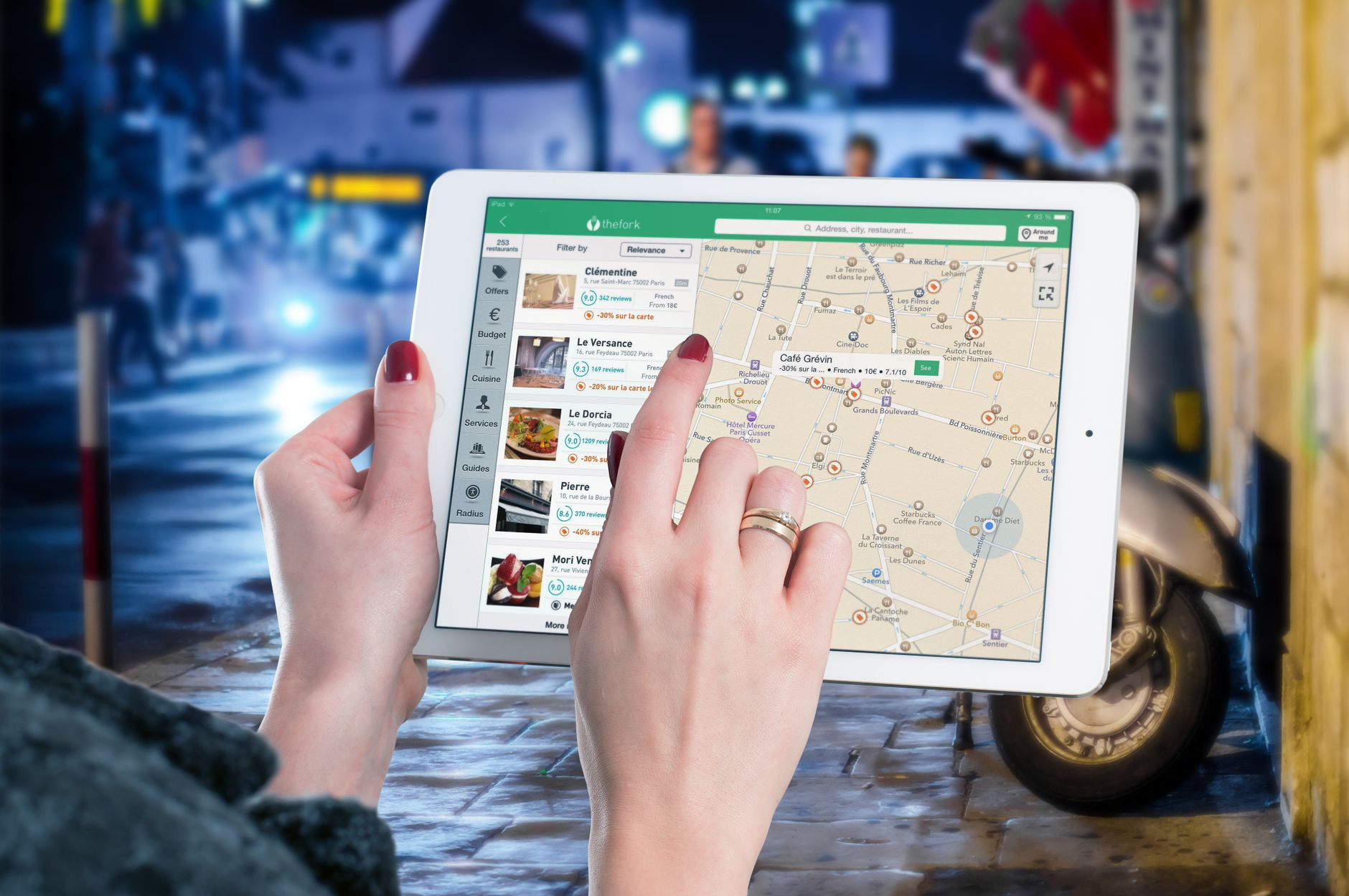 Des mains utilisant une carte numérique sur une tablette dans un milieu urbain la nuit, illustrant la navigation et la technologie.